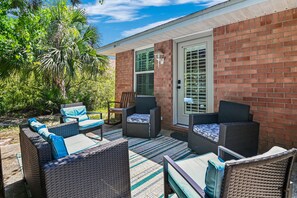 An outdoor patio with wicker furniture, a brick wall, and a door with a window. - ☀️Saltwater Haven | 0.2 Miles to Beach, Pool Access & Pets Welcome☀️ (Miramar Beach)