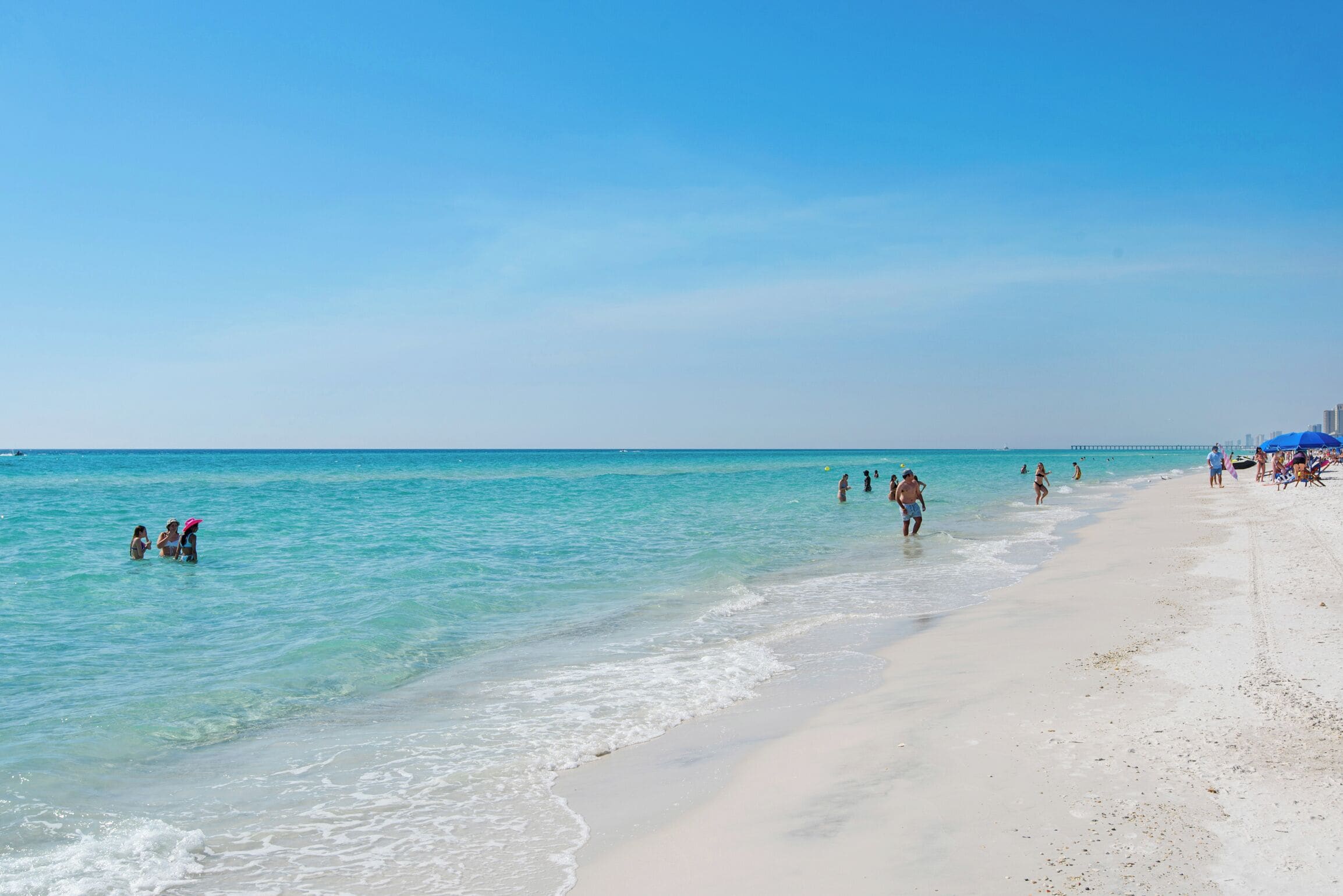 A beach with clear turquoise water, a sandy shore, and people enjoying the water.