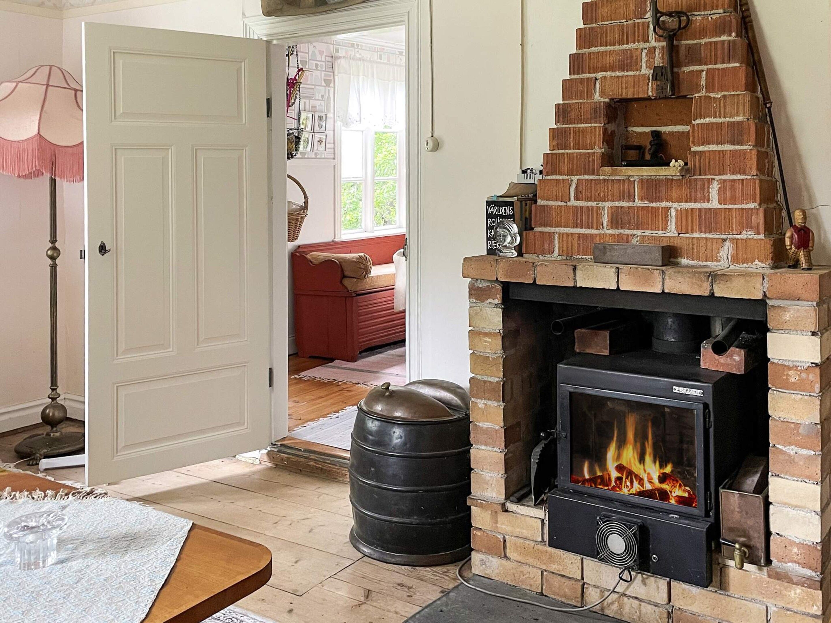 A room with a brick fireplace, a red sofa, and a wooden table with a glass.