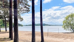 A beach with trees, a volleyball net, and a lake in the background. - 3 Person Holiday Home in Fjardhundra (Fjärdhundra)