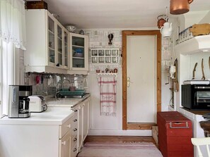A compact kitchen with white cabinets, a coffee maker, a microwave, and a red storage box.