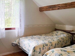 A bedroom with two single beds, a wooden ceiling beam, a window with lace curtains, and a floral bedspread.