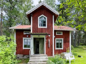 A red wooden house with a green door and white trim, surrounded by greenery.