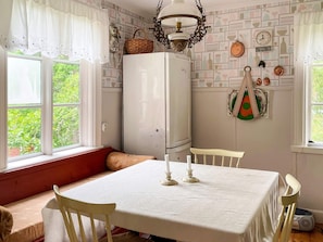 Un coin repas avec une table dressée pour quatre personnes, un réfrigérateur blanc et une fenêtre avec des rideaux.