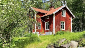 Ett rött trähus omgivet av grönska.