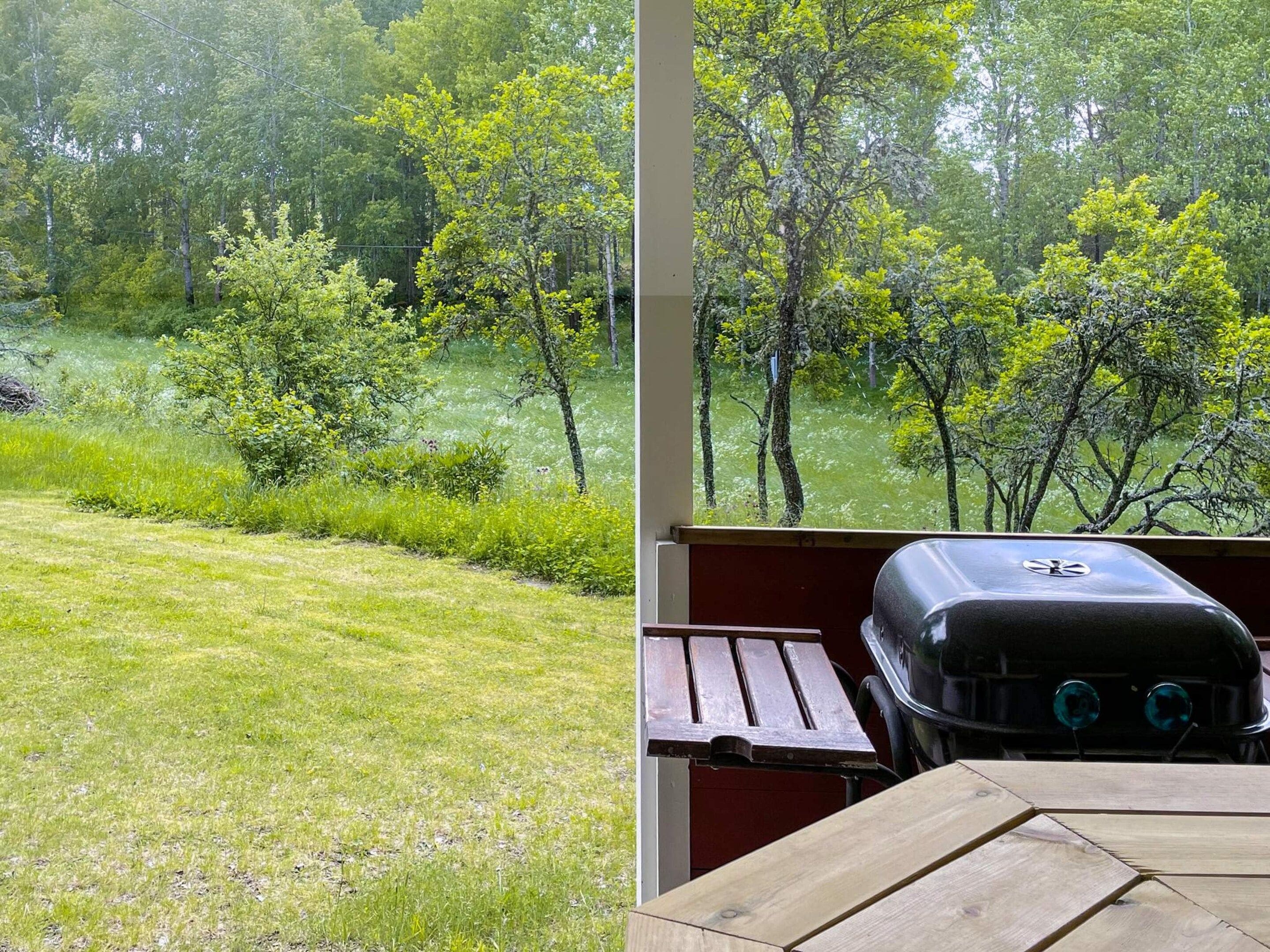 Vista de un área verde con árboles y una parrilla de barbacoa sobre una mesa de madera.
