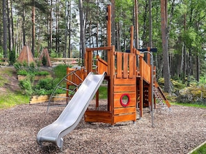 Une aire de jeux avec un toboggan, une structure d’escalade et un élément circulaire rouge.