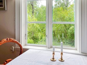 Ein Zimmer mit einem großen Fenster, einem Tisch mit weißem Tuch und zwei Kerzenständern.