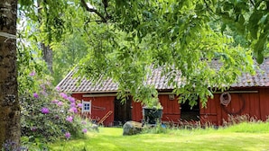 A red wooden house with a tiled roof, surrounded by a well-maintained lawn and flowering plants. - 3 Person Holiday Home in Fjardhundra (Fjärdhundra)