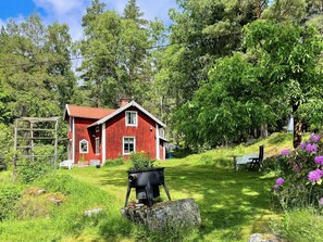 A red house with a wooden deck, surrounded by lush greenery and a barbecue grill. - 3 Person Holiday Home in Fjardhundra (Fjärdhundra)