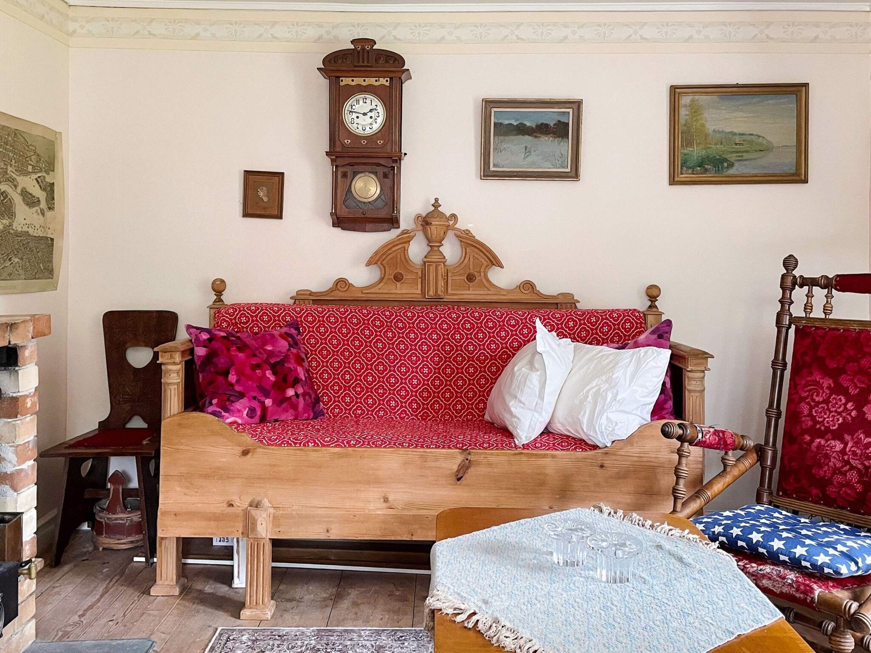 A room with a wooden bed, a wooden chair, a clock, and two framed pictures on the wall.