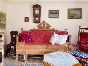 A room with a wooden bed, a wooden chair, a clock, and two framed pictures on the wall.