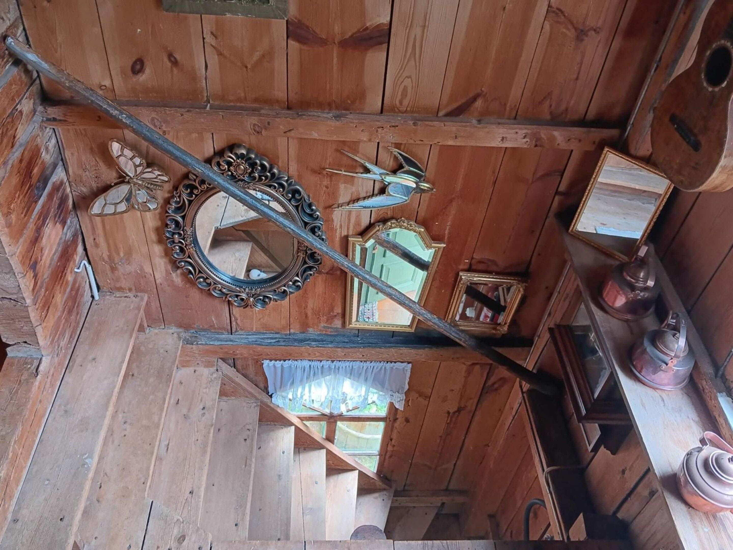 A wooden interior with a mirror, a framed picture, and a shelf with items.