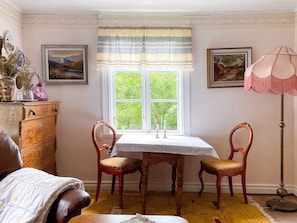 Une pièce comprenant une commode en bois, deux chaises, une table, une fenêtre avec des rideaux et une lampe.