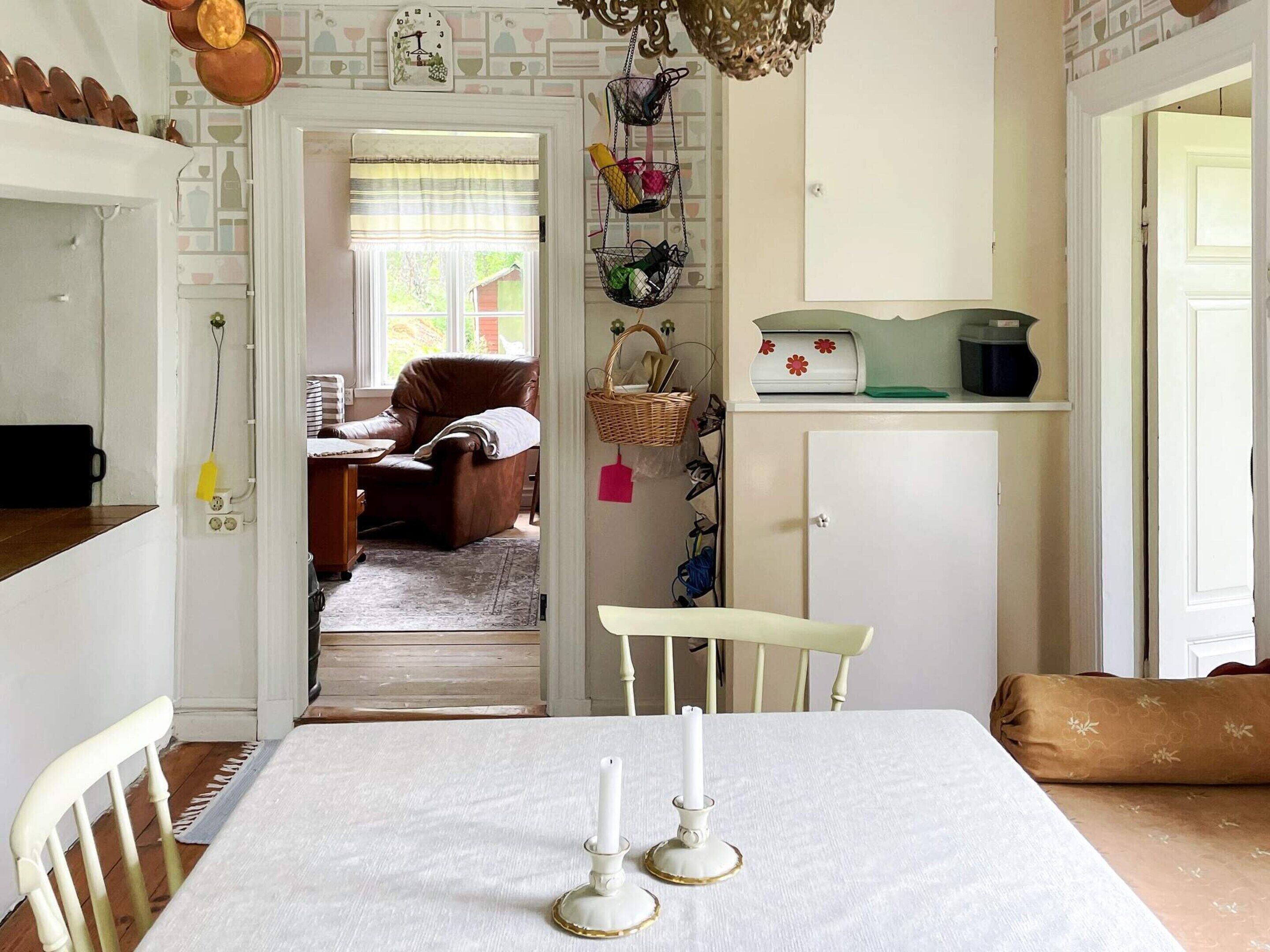 A dining area with a table set for two, a white chair, a brown sofa, and a door leading to another room.
