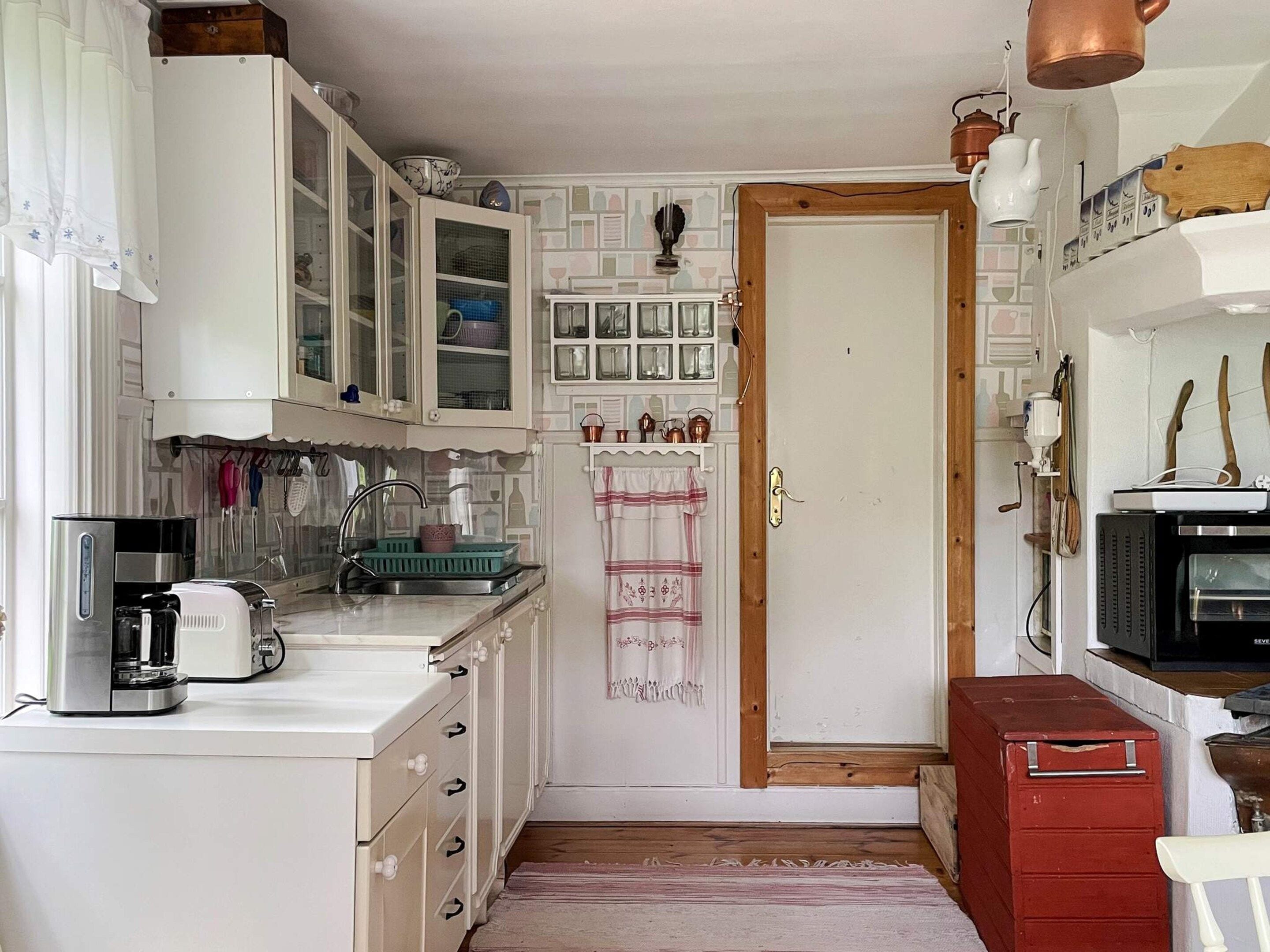 Une cuisine compacte avec des meubles blancs, une machine à café, un four à micro-ondes et un meuble de rangement rouge.