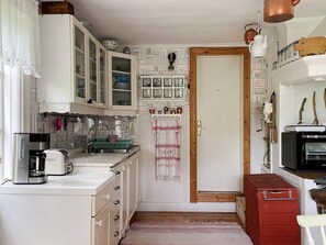 A compact kitchen with white cabinets, a coffee maker, a microwave, and a red storage unit.