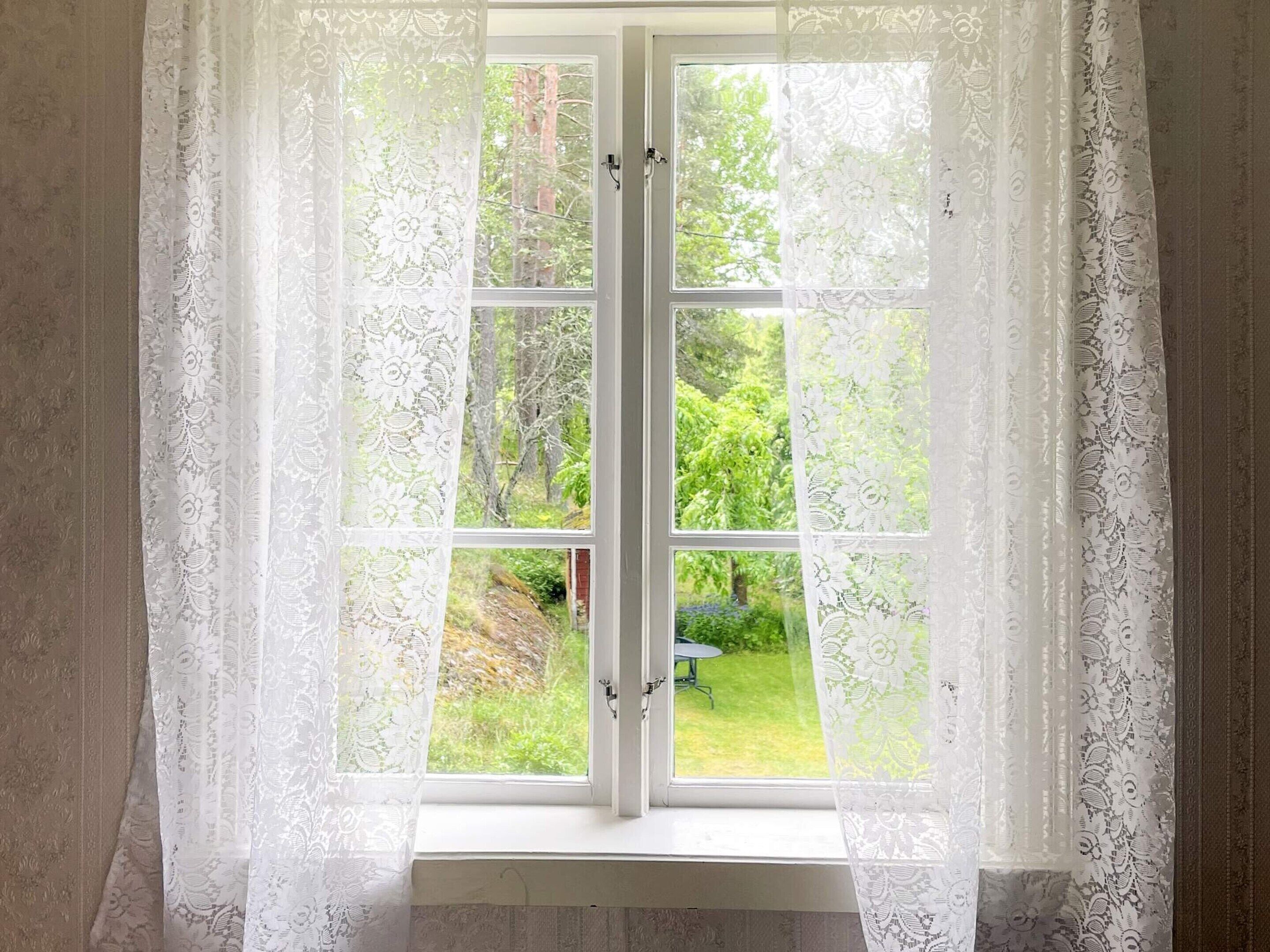 Finestra amb cortines de galeria blanca i vista a un jardí verd.