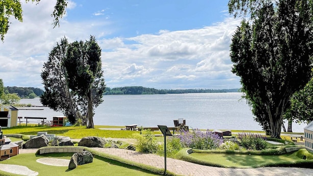 A lakeside view with picnic tables, a small shed, and a well-maintained lawn. - 3 Person Holiday Home in Fjardhundra (Fjärdhundra)