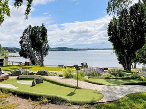 A lakeside view with picnic tables, a small shed, and a well-maintained lawn.
