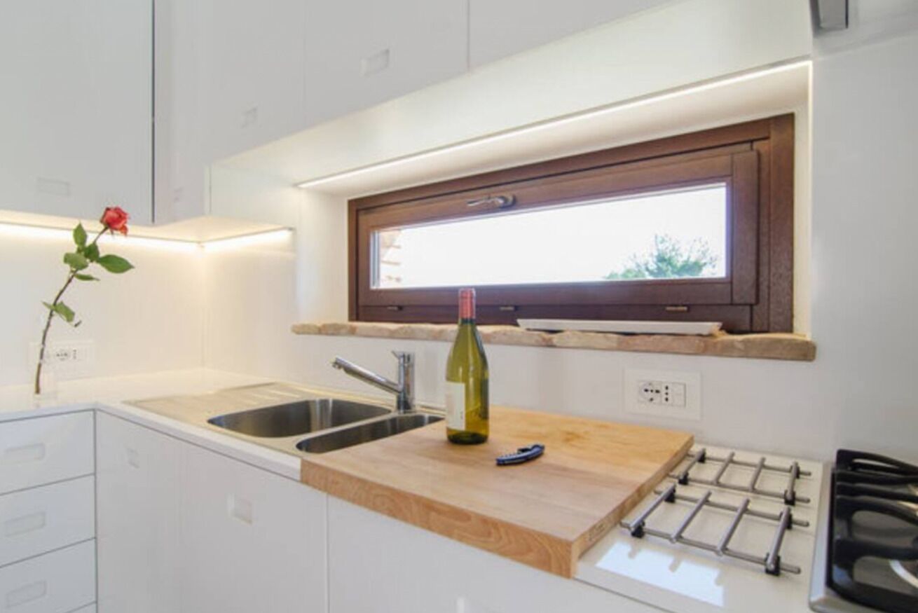 Una cucina moderna con un piano di lavoro in legno, una bottiglia di vino, un lavello e una finestra sopra il piano.