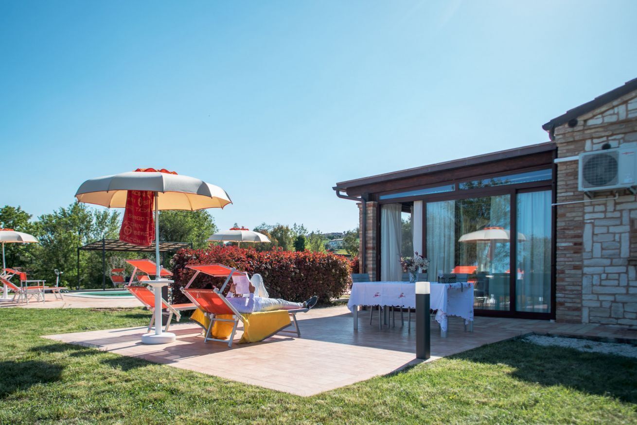 Un'area patio con poltrone da relax e ombrelloni, un edificio con pareti in vetro e un muro in pietra.