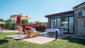 Een terras met lounge stoelen en parasols, een glazen gebouw en een stenen muur.