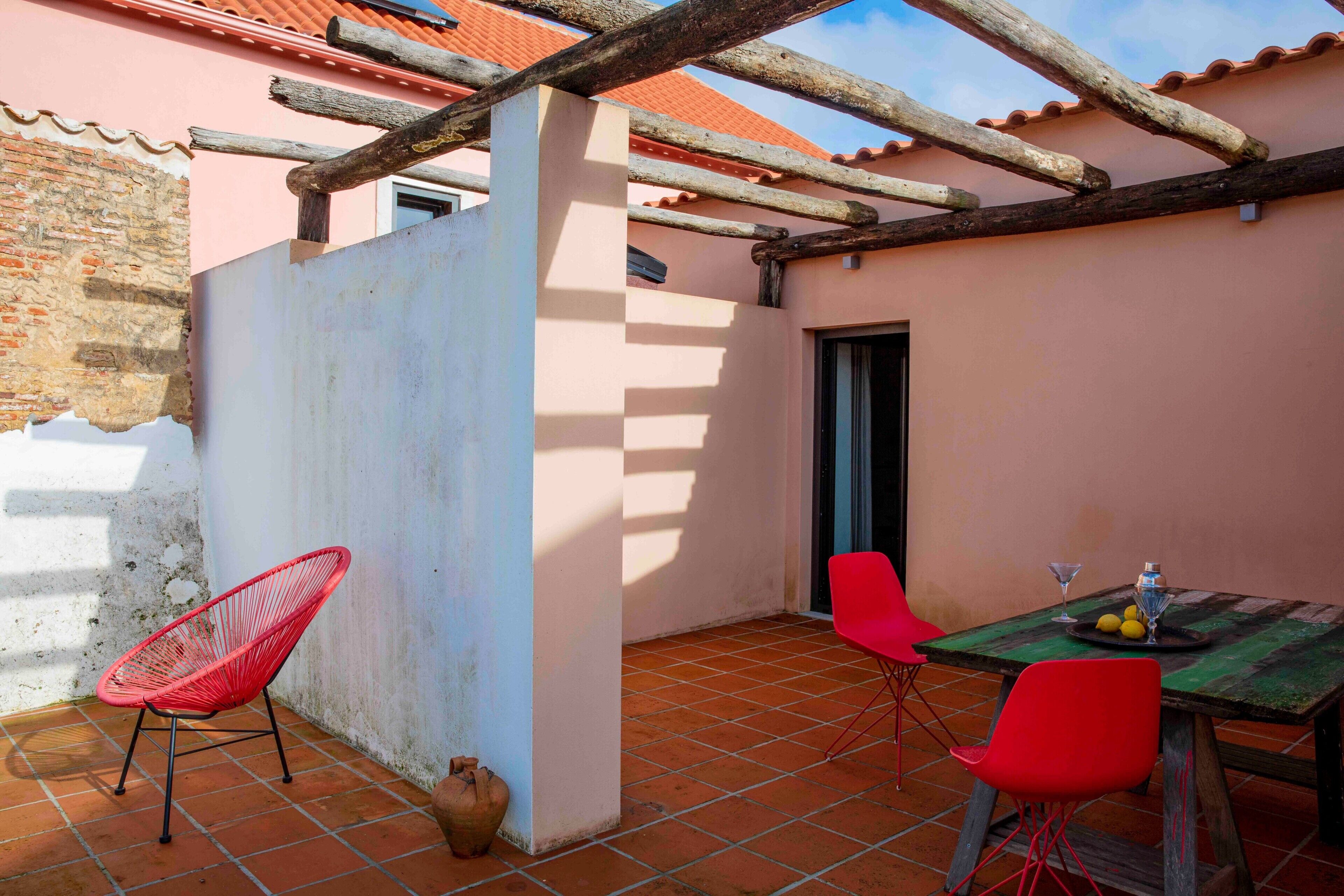 A patio with a table, two red chairs, and a rustic wooden pergola.