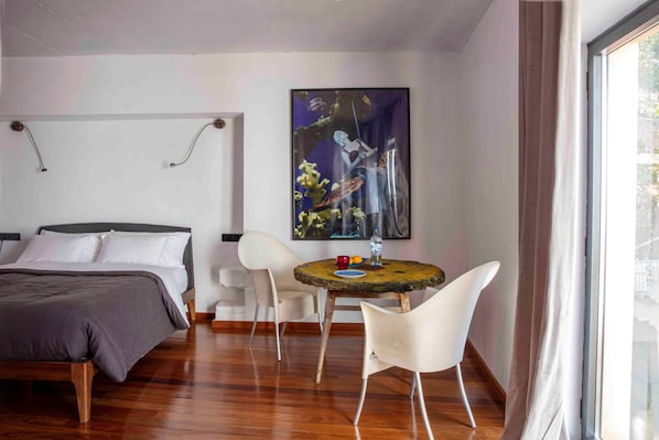 Habitación de hotel con cama, una mesa redonda con sillas, un cuadro en la pared y una ventana con cortinas.
