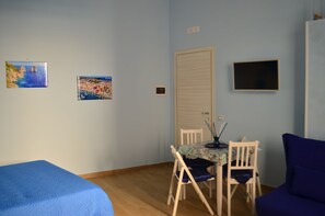 A room with a bed, a dining table with chairs, a TV, and two framed pictures on the wall. - Holiday Home "Solemare Musica & Poesia" (napoli)