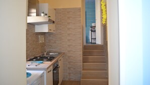 A narrow kitchen with a stove, sink, and cabinets, leading to a staircase. - Holiday Home "Solemare Musica & Poesia" (napoli)