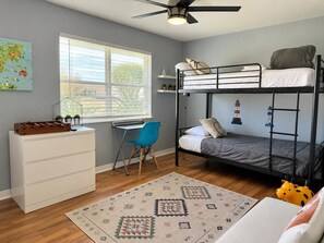 Ein Schlafsaalzimmer mit Etagenbetten, Schreibtisch, Stuhl und einem kleinen Teppich.
