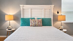 Een bed met een wit hoofdeinde, blauwgroene kussens en een decoratieve plaid.