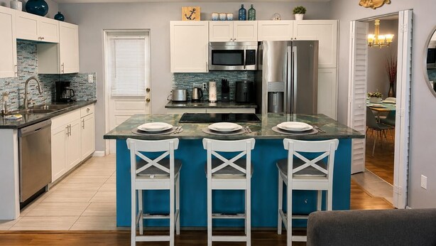 Een moderne keuken met een centraal eiland, witte keukenkastjes en een eethoek met een tafel en stoelen.