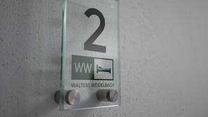 Ein gläsernes Schild mit der Nummer 2, das Zimmernummer, ein Bett-Symbol und den Namen WALTERS WEIDELBACH darunter zeigt.
