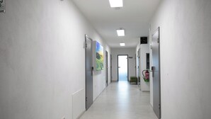 Ein Flur mit weißen Wänden, einem gefliesten Boden und Türen auf beiden Seiten. Eine Feuerlöscher ist an der Wand angebracht.