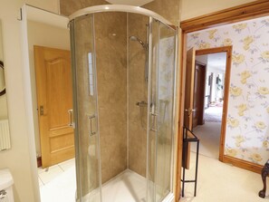 A glass-enclosed shower with a curved design, a wooden door, and a floral wallpaper pattern on the adjacent wall. - Meadow View Bungalow (Droitwich)