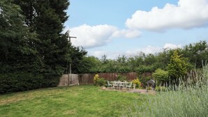Ein Garten mit Holzzaun, Terrassentisch und Stühlen sowie verschiedenen Pflanzen.