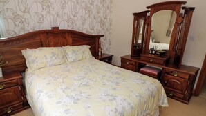 Ein Schlafzimmer mit einem großen Bett, Nachttischen aus Holz, einer Kommode und einem Spiegel.