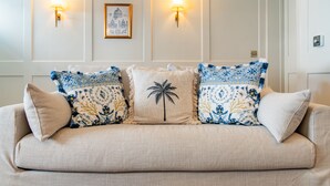 Un sofá color beige con cojines estampados, apliques de pared y un cuadro enmarcado.
