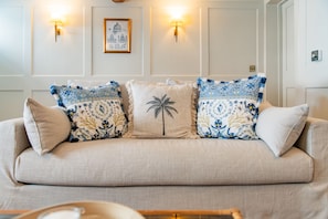 Ein beiges Sofa mit gemusterten Kissen, Wandleuchten und einem gerahmten Bild.
