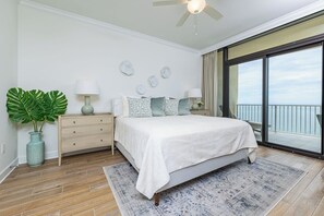 Quarto com cama, mesas de cabeceira, planta em vaso e vista para o oceano.