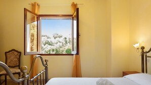 A bedroom with a bed, a chair, a window with curtains, and a wall-mounted lamp. - Holiday Home 'The Pearl Of The Sea' with Mountain View, Private Garden and Wi-Fi (Olbia)