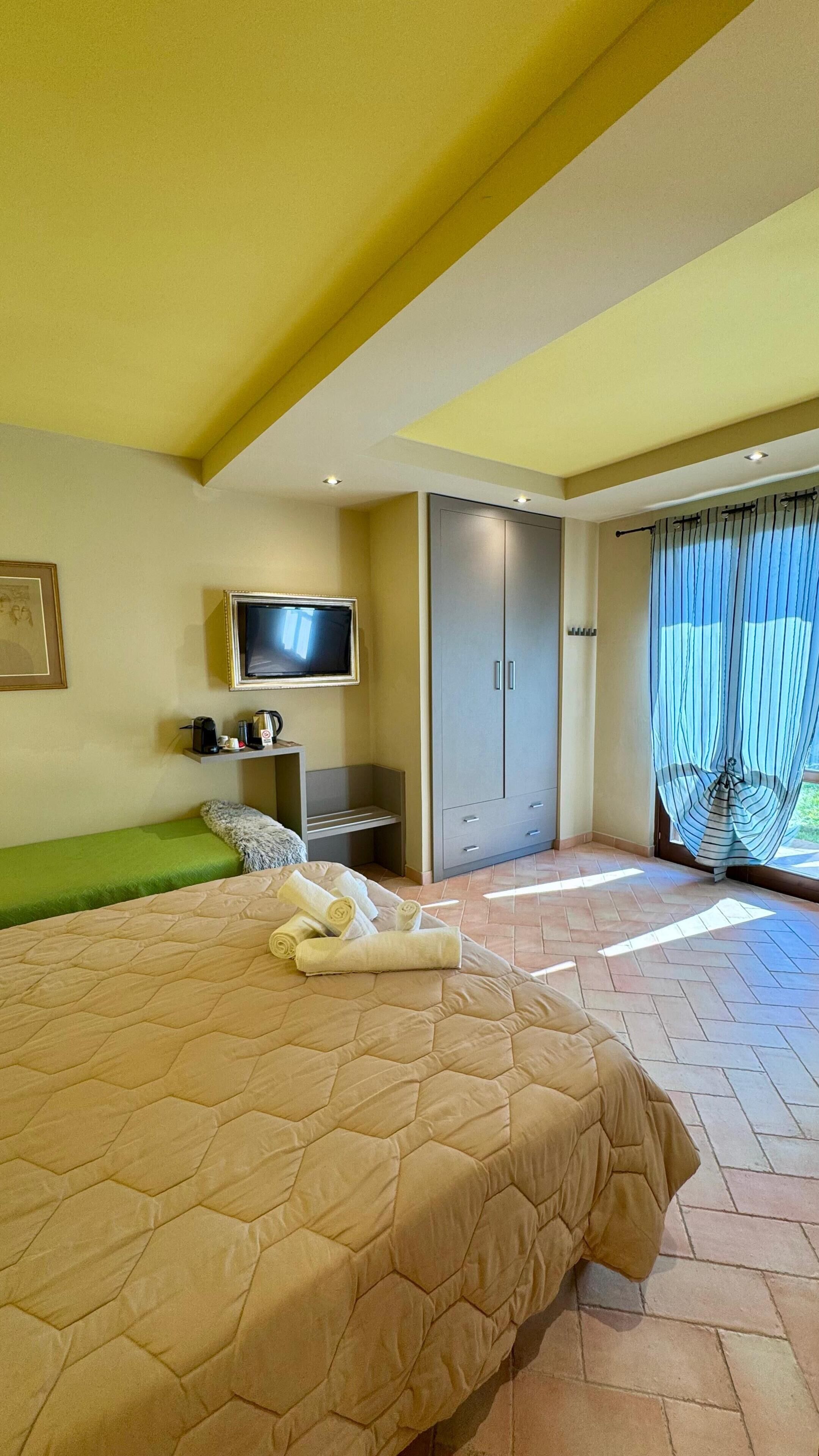 Une chambre à coucher avec un lit, une télévision, une armoire et une fenêtre avec des rideaux.