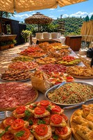 An outdoor buffet with various food items, a thatched umbrella, and a scenic view in the background.
