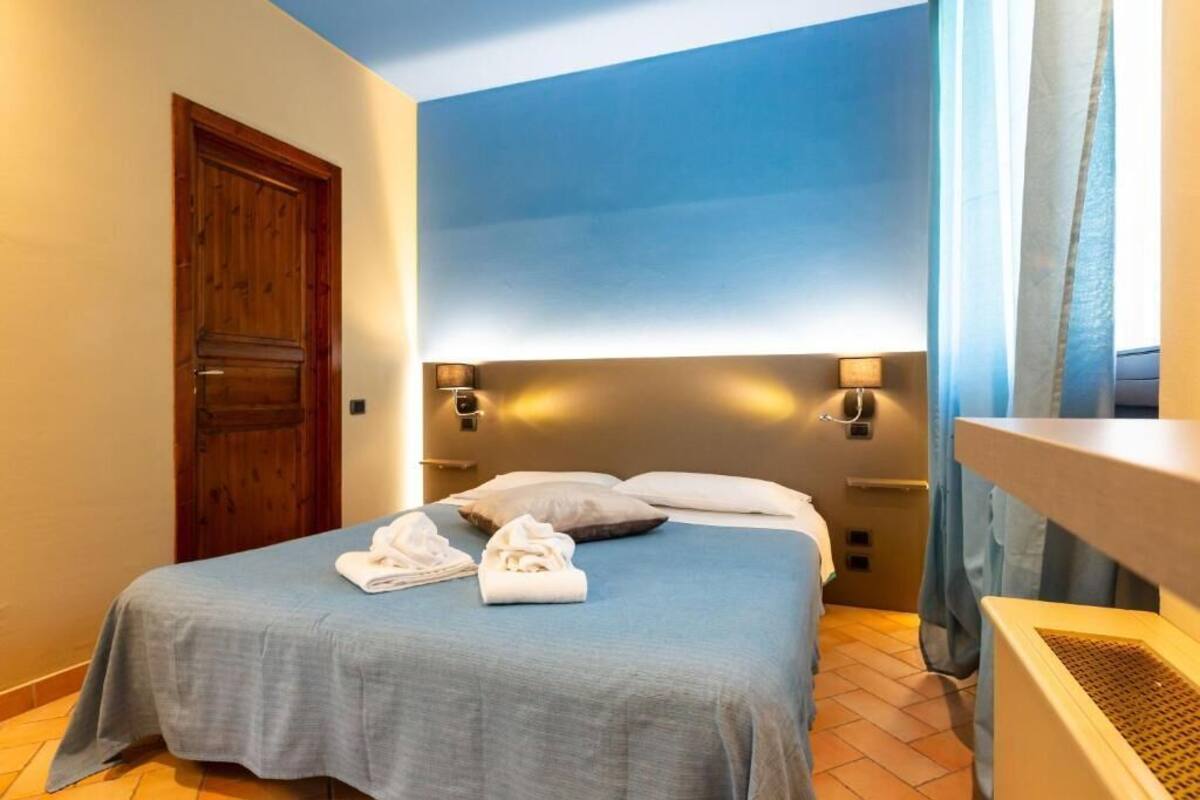 Habitación de hotel con una cama, una puerta de madera y cabecero con luces fijadas a la pared.