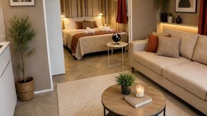 Una sala moderna con sofá, una mesita de centro con un libro y una vela, una cama con cortinas a rayas y una obra de arte urbana en la pared.