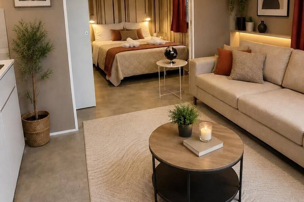 Una sala moderna con sofá, una mesita de centro con un libro y una vela, una cama con cortinas a rayas y una obra de arte urbana en la pared.