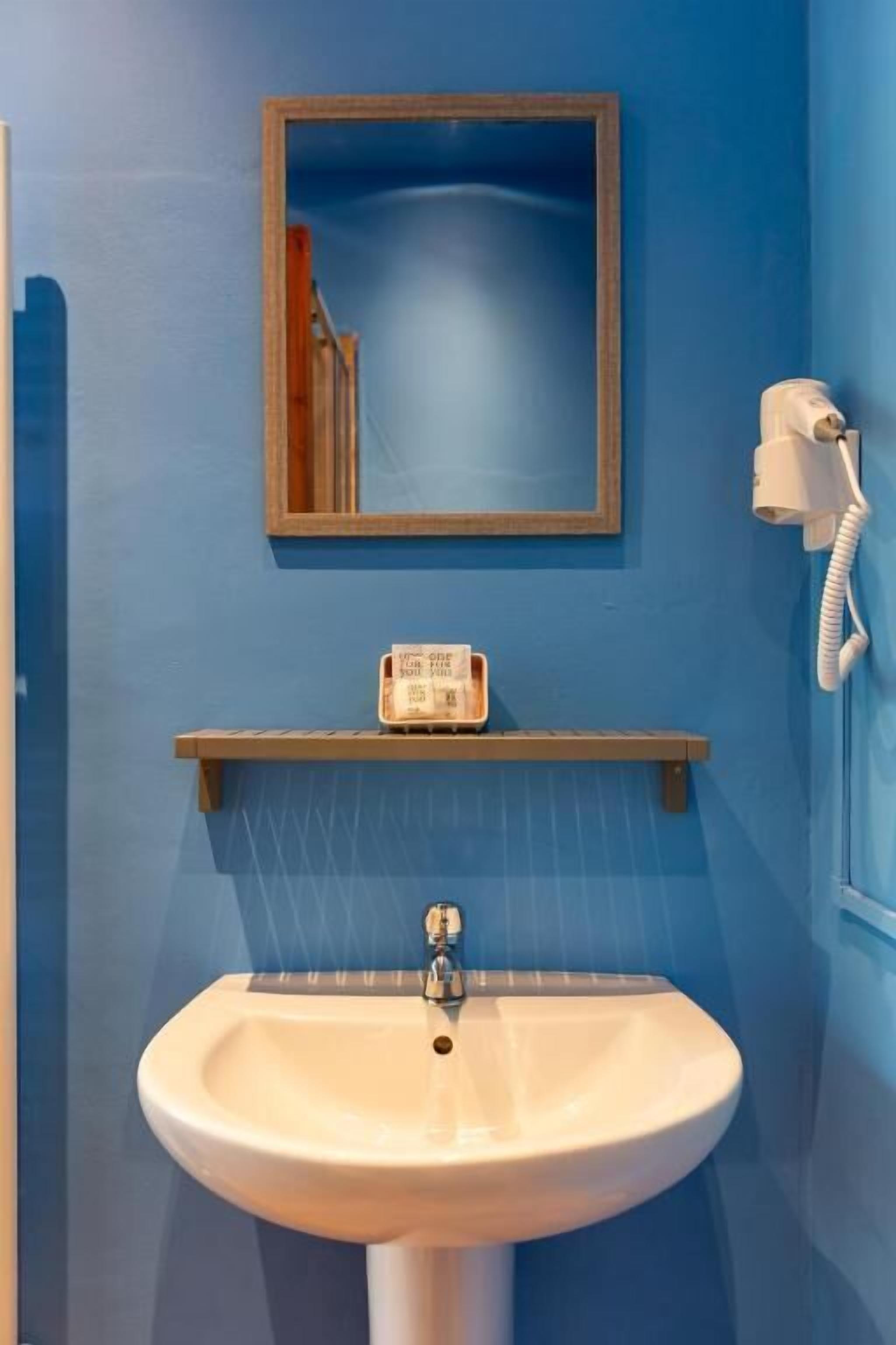 A bathroom with a white sink, a mirror, a telephone, and a shelf with a bottle.