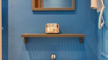 A bathroom with a white sink, a mirror, a telephone, and a shelf with a bottle.